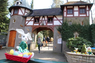Freizeitpark_Sommerrodelbahn_SaisoneröffnungOstern.JPG Ein Osterhase in einem Korb voller bunter Eier vor einem märchenhaften Gebäude mit zwei Türmen.