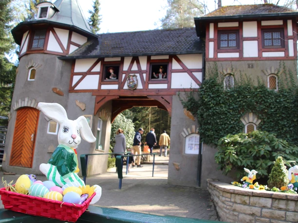 Freizeitpark_Sommerrodelbahn_SaisoneröffnungOstern.JPG Ein Osterhase in einem Korb voller bunter Eier vor einem märchenhaften Gebäude mit zwei Türmen.