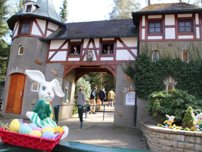 Freizeitpark_Sommerrodelbahn_SaisoneröffnungOstern.JPG Ein Osterhase in einem Korb voller bunter Eier vor einem märchenhaften Gebäude mit zwei Türmen.