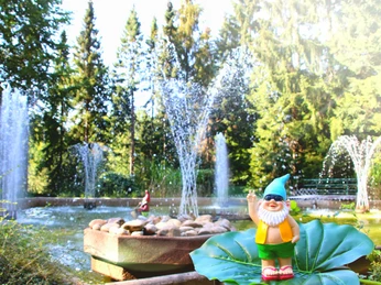 Ibbenbüren_Sommerrodelbahn_Wasserspiele_Freizeitpark_Sommerrodelbahn.jpg Ein Garten mit Wasserspielen, umgeben von Bäumen, im Vordergrund ein fröhlicher Gartenzwerg.