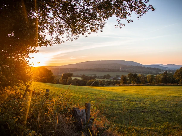 Rischenau_Sonnenuntergang.jpg Weite Wiesen mit vereinzelten Bäumen bei Sonnenuntergang, sanfte Hügel im Hintergrund.
