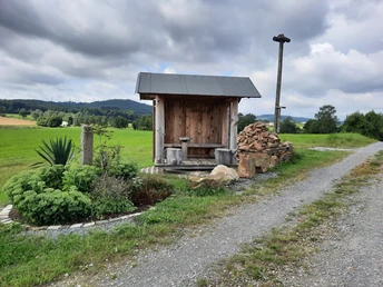 Klosterhütte Falkenhagen Eine rustikale Holzhütte mit Sitzbank am Wegesrand, umgeben von grünen Feldern und Hügeln.