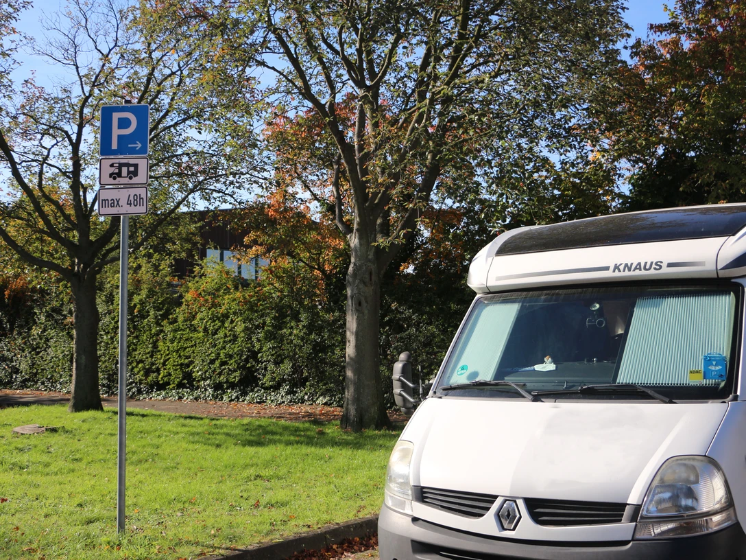 Wohnmobilstellplatz am Jahnstadtion in Langenfeld Wohnmobilstellplatz mit Parkplatzschild für max. 48h, umgeben von Bäumen und grünem Rasen.