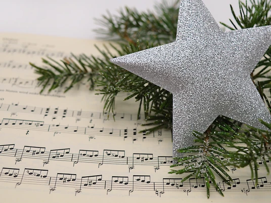 Notenzettel daneben ein Tannenzweig und einem glitzernden Stern.