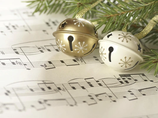 Goldene und weiße Weihnachtsglöckchen liegen auf einem Blatt mit gedruckten Musiknoten unter Zweigen.