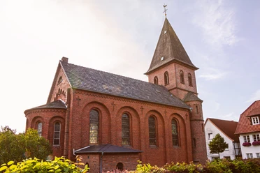 St.Johannis Kirche Backsteinkirche St. Johannis mit spitzem Turmdach und Rundbogenfenstern, umgeben von grünen Büschen.