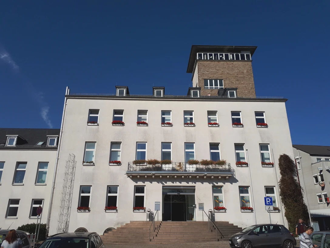 Rathaus Velbert Rathaus Velbert mit imposantem Turm, weißen Fassaden und rot-blühenden Fensterkästen bei blauem Himmel.