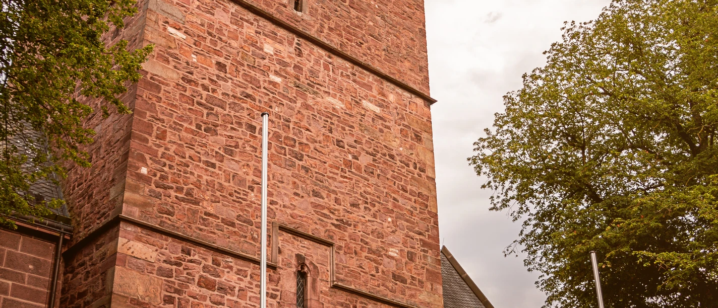 Backsteinkirche von St. Marien in Lügde mit markantem Turm, hellem Himmel und großen Bäumen.