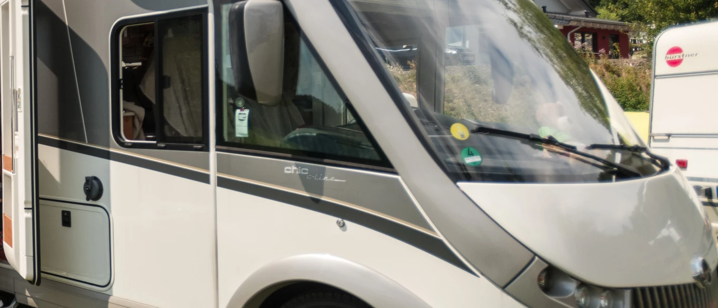 Symbolbild Wohnmobil.jpg Frontansicht eines geparkten, modernen Wohnmobils mit großen Fenstern auf einer grünen Wiese.