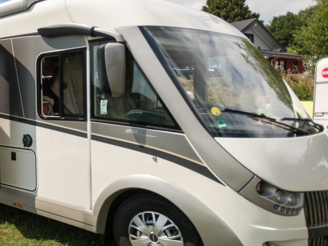 Symbolbild Wohnmobil.jpg Frontansicht eines geparkten, modernen Wohnmobils mit großen Fenstern auf einer grünen Wiese.