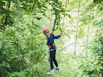 Kletterpark Interakteam_Teutoburger Wald_Leon Neufeld_CCBYSA.jpg Ein junger Kletterer balanciert auf einem Seilparcours in einem grün bewachsenen Kletterpark.