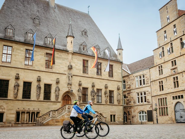 Rad-Event auf der Friedensroute Zwei Radfahrer vor einem historischen Sandsteingebäude mit Skulpturen.