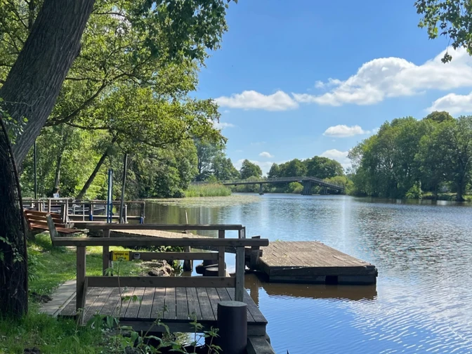 Anleger Melchers Hütte Holzanleger an der Hamme bei Melchers Hütte mit Blick auf Fluss, Bäume und Brücke im HintergrundCanoe and peat boat mooring at the Melchers Hütte restaurantAanlegplaats voor kano's en turfboten bij restaurant Melchers HütteFortøjning af kano og tørvebåd ved restauranten Melchers Hütte