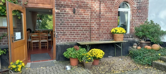 Bauernhof-Café Groß Ilbeck in Ratingen Eingang eines roten Backsteingebäudes mit offenen Holztüren, blühenden gelben Chrysanthemen in Körben.