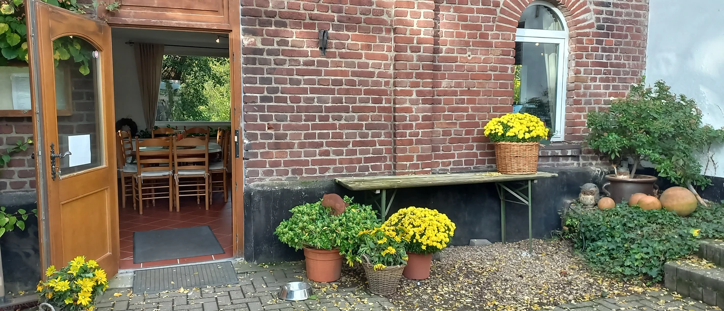 Bauernhof-Café Groß Ilbeck in Ratingen Eingang eines roten Backsteingebäudes mit offenen Holztüren, blühenden gelben Chrysanthemen in Körben.