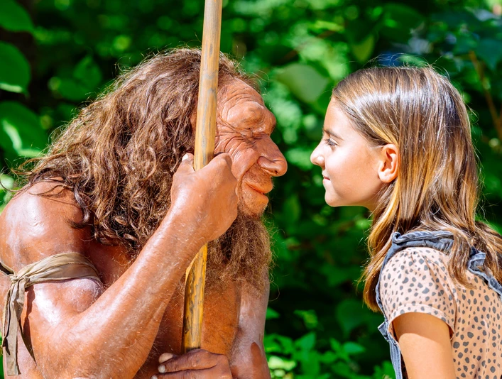 Gesichtervergleich mit MR N und Mädchen Ein Mädchen steht einem Neandertaler-Modell gegenüber, beide blicken sich intensiv in die Augen.