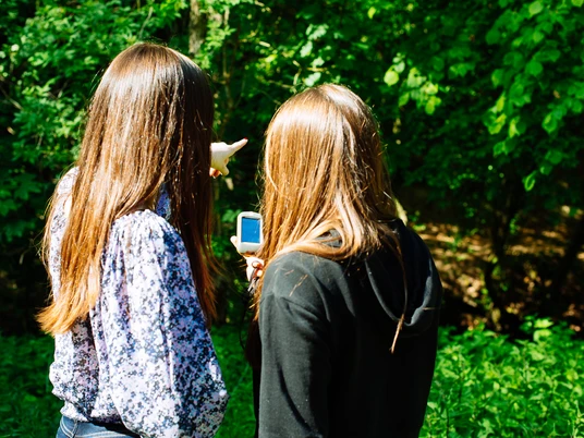 Geocaching im Neandertal Zwei Personen erkunden mit einem Navigationsgerät einen Wald, umgeben von üppigem Grün.