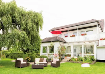 Das Zweistöckige Nethegau Haus von außen mit Sitzgelegenheiten und einem Baum draußen im Garten.