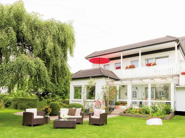 Das Zweistöckige Nethegau Haus von außen mit Sitzgelegenheiten und einem Baum draußen im Garten.