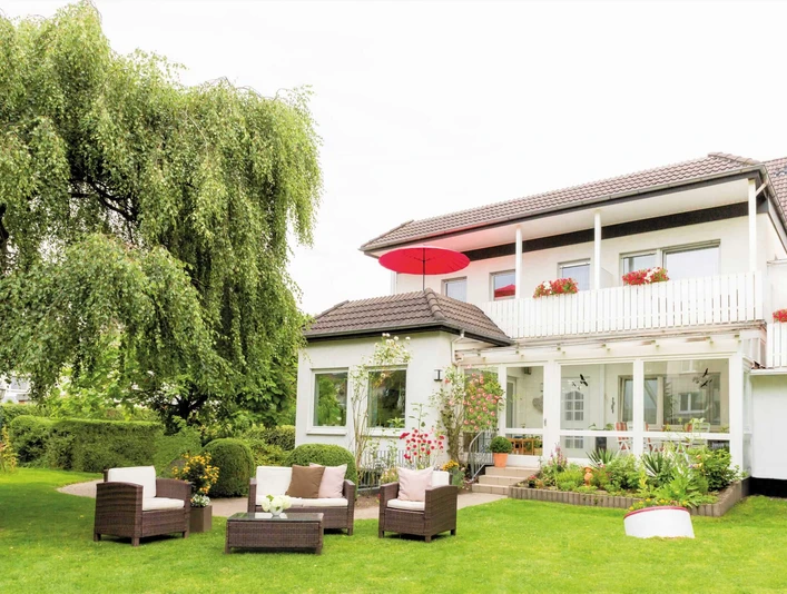 Das Zweistöckige Nethegau Haus von außen mit Sitzgelegenheiten und einem Baum draußen im Garten.