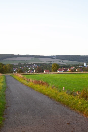 Ausblick Rischenau Weitläufige Landschaft mit einem Weg, der zu einem Dorf inmitten von grünen Feldern führt.