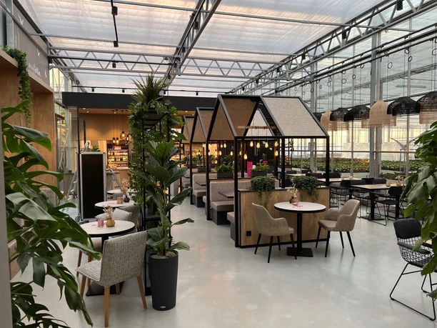 Café Karl Nienburg Geräumiges Café mit moderner Einrichtung, grünen Pflanzen und gemütlichen Sitznischen in Gewächshaus-Optik.