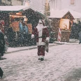Weihnachtsmann - Weihnachtsmann_BLUR.jpg Der Weihnachtsmann geht durch einen verschneiten Weihnachtsmarkt, umgeben von Holzhütten und Besuchern.