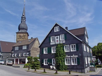 Wermelskirchen Fachwerkhäuser mit Schindelfassaden und ein steiler Kirchturm prägen eine malerische Straßenszene.