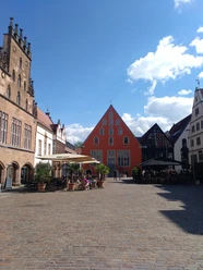 Lemgo_Innenstadt_BildSalzuflen_CC_BY_SA_Teutoburger_Wald_Kerstin_Paar_IMG_20220613_163607_206.jpg Ein belebter Platz in Lemgo mit historischen Fachwerkhäusern und zahlreichen Besuchern bei Sonnenschein.