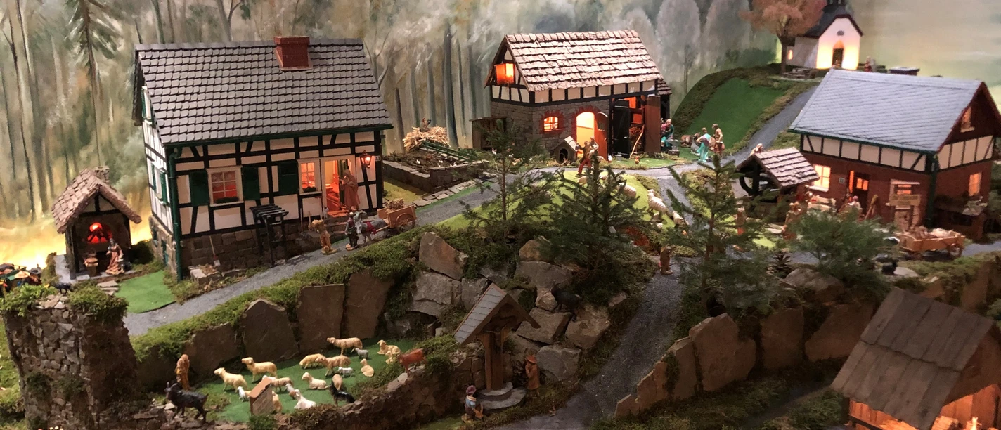 Heimatkrippe Much Idyllisches Miniaturdorf, Fachwerkhäuser, grüner Hügel, Schafe, Kirche im Hintergrund, detailreich gestaltet.