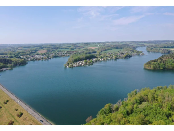 Campingpark Luftaufnahme eines großen, blauen Sees, umgeben von grünen Wäldern und kleinen Siedlungen.