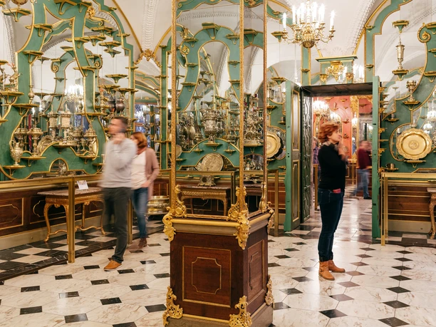 SKD_Schloss_Image_MG_4530_davidpinzer_kleiner_1611.jpg Besucher in einem prächtigen Raum im Grünen Gewölbe, mit verzierten Vitrinen und historischen Objekten.