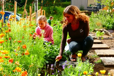 Umweltbildungszentrum Heiligenhaus Zwei Personen arbeiten in einem farbenfrohen Garten voller blühender Blumen bei Sonnenlicht.