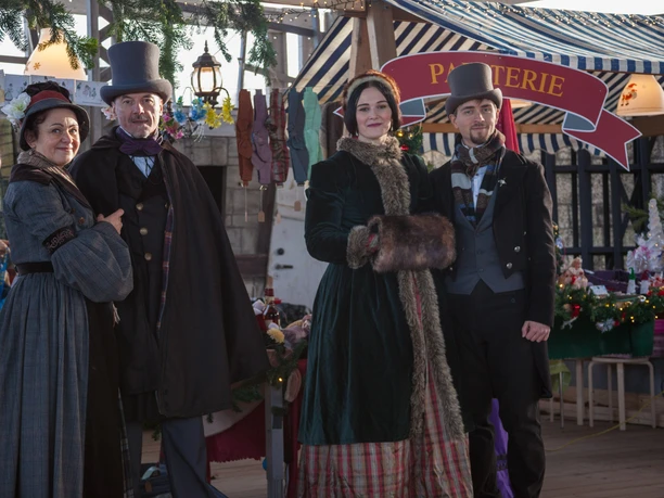 Viktorianischer Weihnachtsmarkt am Biedermeierstrand - Weihnachten in der Region Leipzig Vier Personen in viktorianischer Kleidung vor einem festlich geschmückten Verkaufsstand.