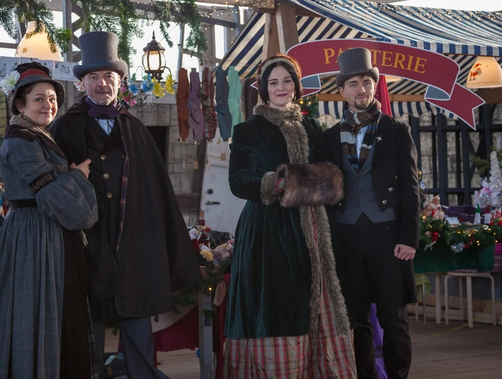 Viktorianischer Weihnachtsmarkt am Biedermeierstrand - Weihnachten in der Region Leipzig Vier Personen in viktorianischer Kleidung vor einem festlich geschmückten Verkaufsstand.