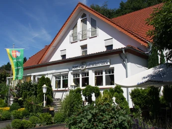 Das Hotel Hubertushof präsentiert sich vor weißer Fassade mit roten Dachschindeln und gepflegtem Garten.
