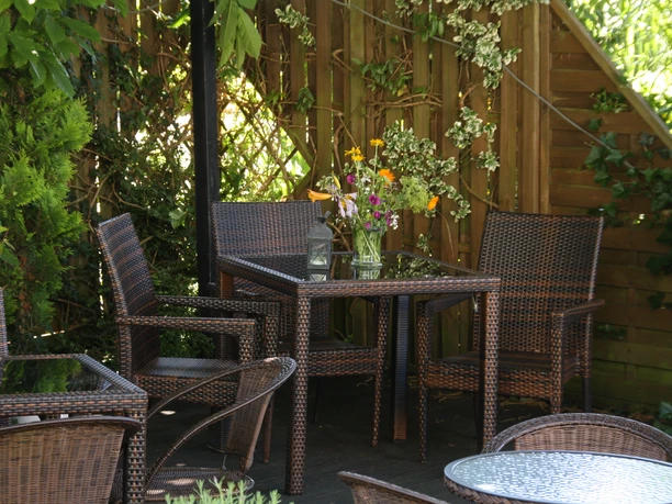Hotel Hubertushof Rattan-Gartenmöbel unter einem Sonnenschirm um einen Tisch mit buntem Blumenstrauß im Grünen.