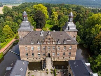 Schloss Hugenpoet Luftaufnahme von Schloss Hugenpoet mit seinen zwei markanten Türmen, umgeben von üppigem Grün.