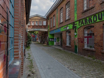 Weberei Gepflasterte Gasse zwischen Backsteingebäuden mit bunten Graffitis und grünem "Parkour"-Schild.