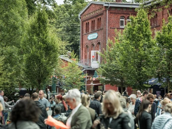 Historisches rotes Backsteingebäude bei einer belebten Freiluftveranstaltung mit vielen Besuchern.