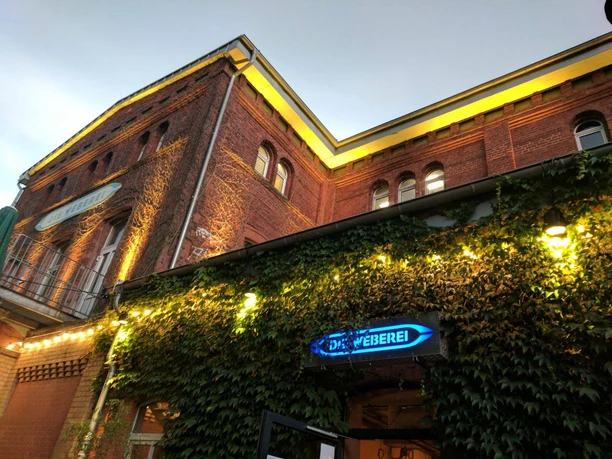 Die Weberei Historisches Backsteingebäude mit bewachsener Fassade und leuchtendem Schild "Dampfbierbrauerei".