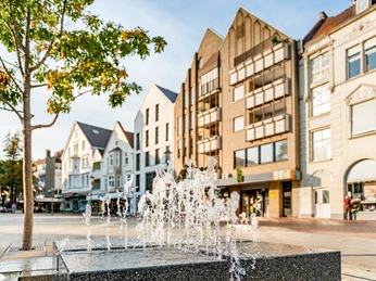 Wasserband Berliner Platz Belebter Platz mit modernen Gebäuden im Hintergrund und einem sprudelnden Brunnen im Vordergrund.