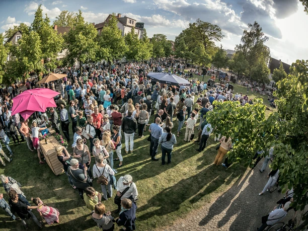 Eine große Menschenmenge versammelt sich bei einem sonnigen Freiluft-Event in einem grünen Park.