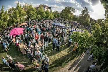 Freitag 18 Dreiecksplatz Eine große Menschenmenge versammelt sich bei einem sonnigen Freiluft-Event in einem grünen Park.