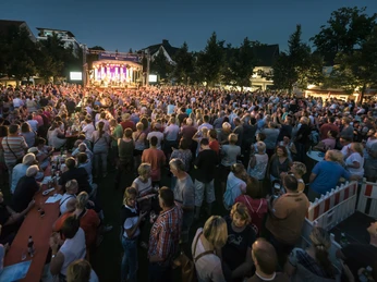 Dreiecksplatz Gütersloh Eine große Menschenmenge genießt ein Open-Air-Konzert im Freien bei Einbruch der Dämmerung.