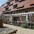 Außenbereich vom Alten Brauhaus zu Fallersleben Der Außenbereich des Alten Brauhauses zu Fallersleben zeigt einen gemütlichen Biergarten mit Holztischen unter einer Pergola. Links ist ein kleiner Holzspielplatz auf sandigem Boden zu sehen. Der Backsteinbau im Hintergrund trägt ein rotes Ziegeldach mit Gauben.