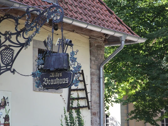 Altes Fachwerkhaus mit verziertem schmiedeeisernem Schild in ruhiger, grüner Umgebung.