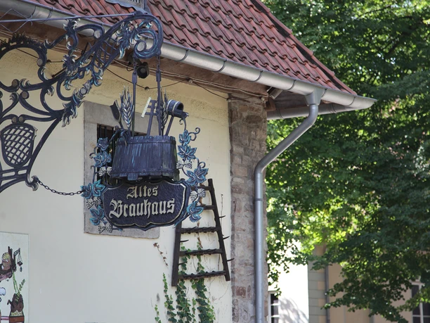 Old half-timbered house with ornate wrought-iron sign in quiet, green surroundings.