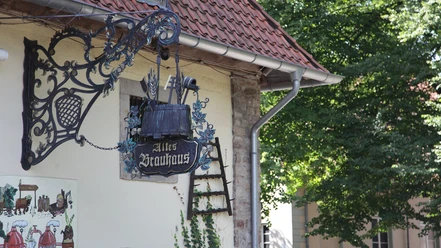 Altes Brauhaus zu Fallersleben Altes Fachwerkhaus mit verziertem schmiedeeisernem Schild in ruhiger, grüner Umgebung.
