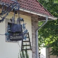Altes Brauhaus zu Fallersleben Altes Fachwerkhaus mit verziertem schmiedeeisernem Schild in ruhiger, grüner Umgebung.